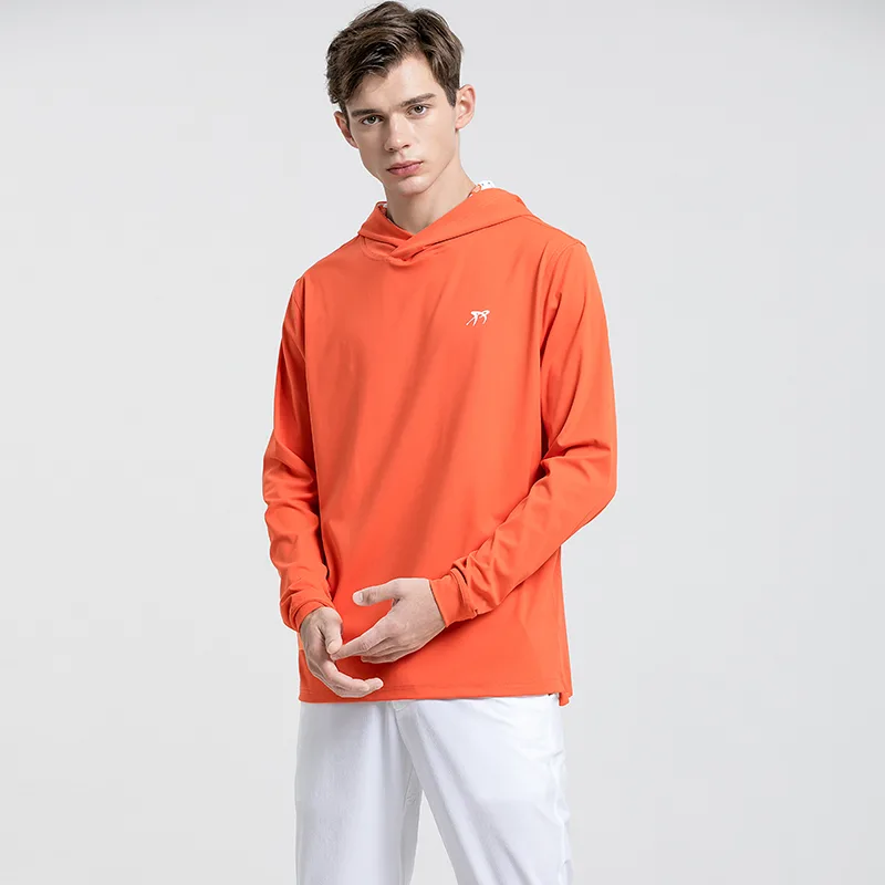 Man in orange hoodie and white pants standing.